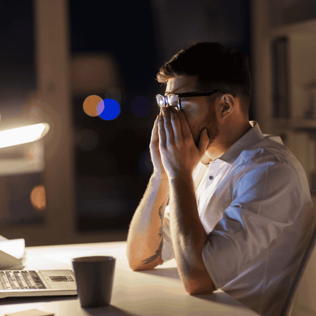 Frustrated man working late at night on EB5 investment, stressed about visa or immigration process, in an office environment.