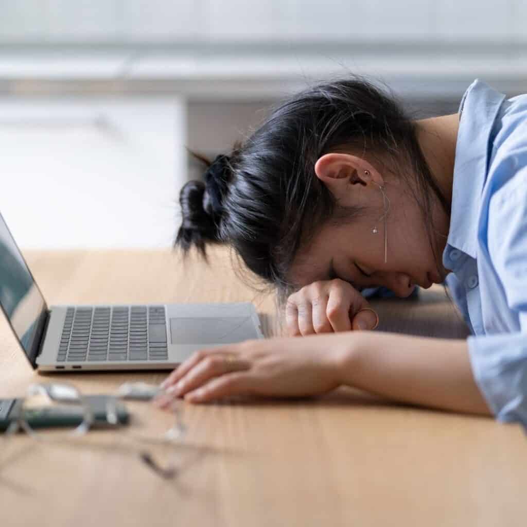 Frustrated woman with head on desk near laptop, feeling stressed or overwhelmed, representing challenges in EB-5 investment process in Houston.